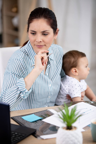 wielozadaniowy biznes kobieta siedzi z jej dziecko w biurze - Zdjęcie, obraz