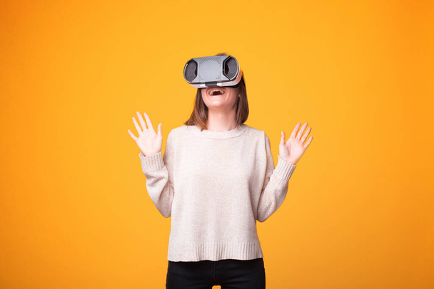 Hämmästynyt nuori nainen seisoo keltainen tausta ja ottaa Virtual Reality Experience - Valokuva, kuva