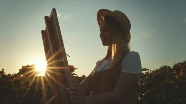 Μια γυναίκα ζωγραφίζει με μια βούρτσα στον καμβά. Ο πίνακας στέκεται πάνω σε ένα καβαλέτο. Φοράει καπέλο. Κοντινό πλάνο. 4K - Πλάνα, βίντεο