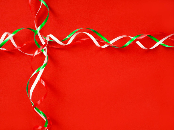 Christmas concept - thin Christmas ribbons of colors: white, red, green, are on a red background, like on a gift box - Photo, image