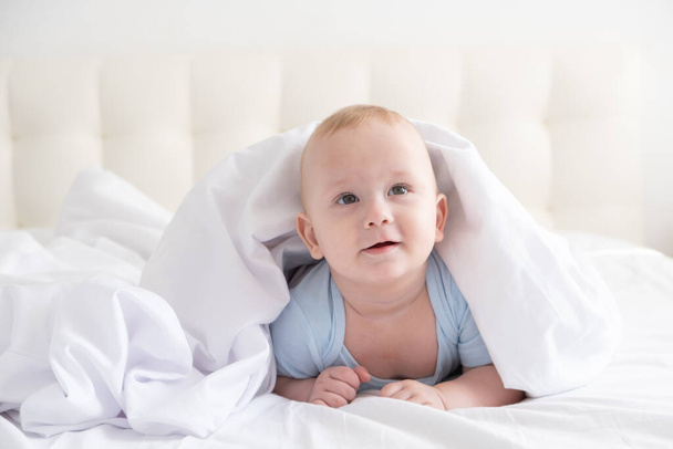 面白い赤ちゃんが笑顔で家の白い寝具に横になって.  - 写真・画像