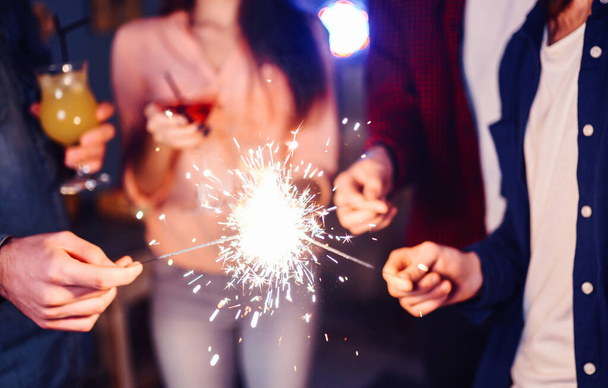 Christmas sparkles in hands. A crowd of young happy people with sparklers in their hands during celebration. Sparkling lights of bengal fires 2021. - Foto, Imagen