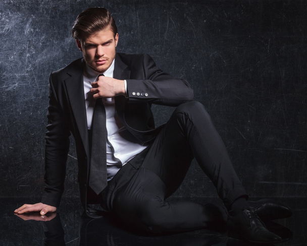 сидячий чоловік моди фіксує свою чорну краватку
 - Фото, зображення