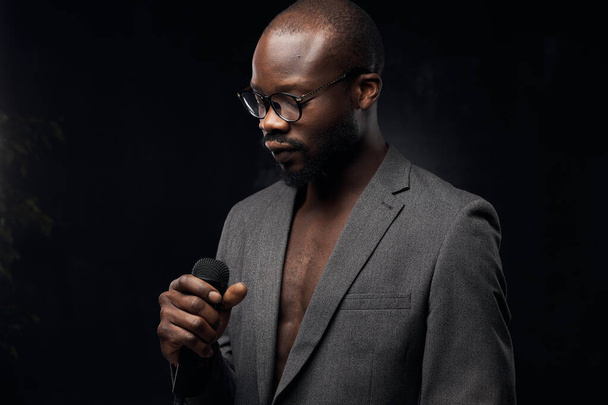 portrait of a dark-skinned handsome guy with a beard on a black background, singing in a microphone  with closed eyes  - Foto, immagini