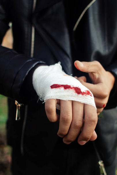 Man with bandage with blood on the knuckles, natural background. End of fight, fight, blood and aggression concept. A man in a leather jacket. - Photo, Image