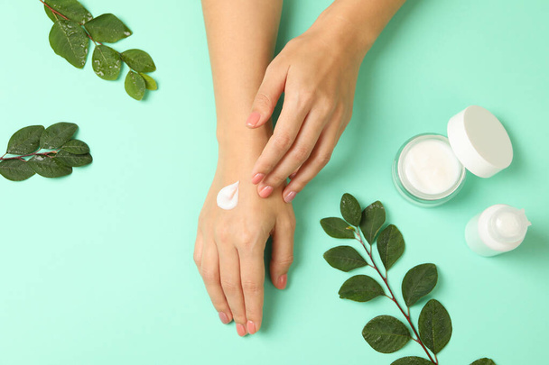 Female hands with cosmetics cream on mint background - Photo, image