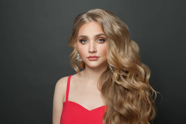 Blondýny žena celebrity s make-upem a dlouhé kudrnaté účes v červené večerní šaty na černém pozadí - Fotografie, Obrázek