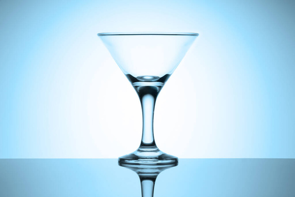 Üres martinis üveg áll egy fényes asztalon tükröződéssel. Hidegkék színű matrica. - Fotó, kép