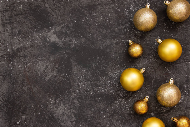 Prachtige gouden kerstballen en een sparren tak op een donker zwarte achtergrond. Vlak ontwerp. Kopieerruimte. - Foto, afbeelding