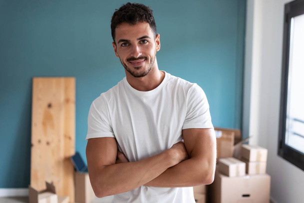 Shot of handsome young man standing looking at camera while resting from making boxes for the move to new apartment. - Foto, Imagen