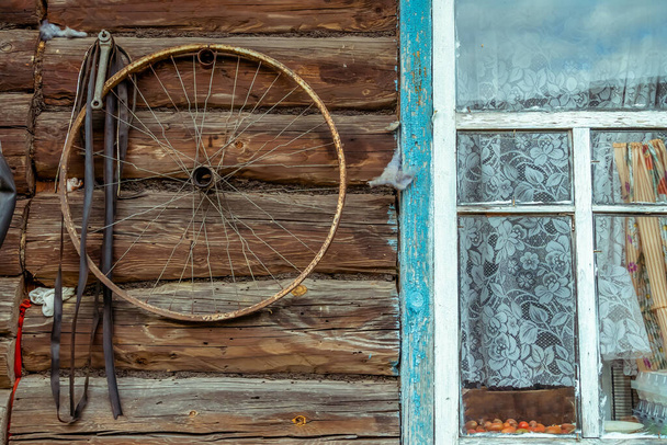 Fahrradrad hängt an der Wand eines alten Holzhauses mit altem Fenster - Foto, Bild