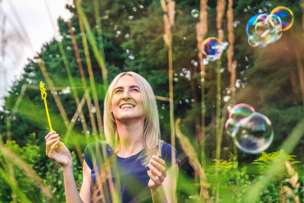 Young beautiful blonde woman blowing soap bubbles in the Park. - Foto, immagini