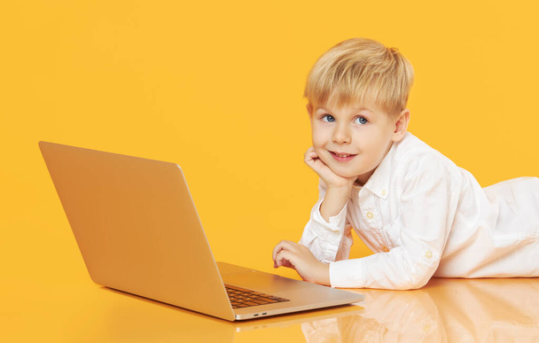 Litttle child boy using laptop on yellow background. Education, online study, home studying, distance learning. Primary school student during quarantine - Valokuva, kuva