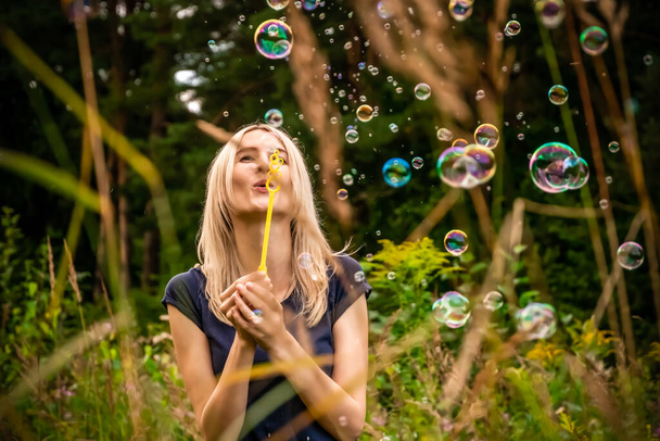 Mladá krásná blondýna žena foukání mýdlo bubliny v parku. - Fotografie, Obrázek