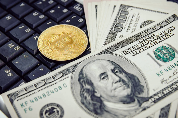 ビットコインはラップトップのキーボードの上に横たわっており、米ドルの束がクローズアップされています。ビジネスと商業の概念. - 写真・画像