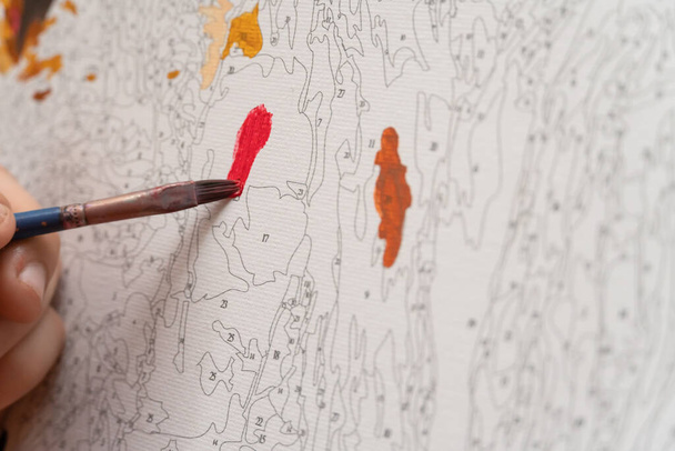 la mano del niño pinta el cuadro por los números se cierran con el pincel rojo - Foto, Imagen