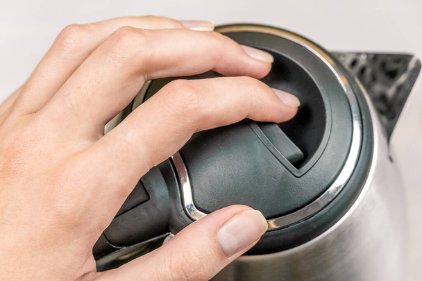 woman's hand holds the black lid of a gray electric kettle on a light table close up - Photo, Image