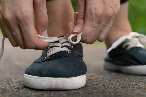 Close-up van de handen van vrouwen veters strikken in donkerblauwe sneakers op een jog in het bos. - Foto, afbeelding