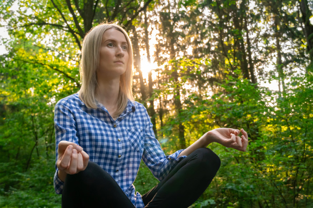 Młoda piękna blondynka siedzi w pozycji Lotusa na sportowej macie w lesie o zachodzie słońca. koncepcja zdrowego stylu życia. Portret - Zdjęcie, obraz
