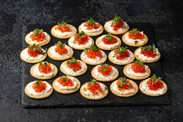 Caviar de salmón y galletas saladas de queso blando con semillas de sésamo y amapola servidas en pizarra negra - Foto, Imagen