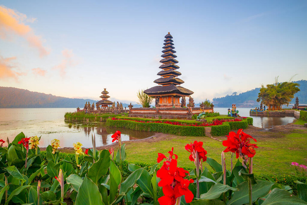Chrám Pura Ulun Danu Bratan na ostrově Bali. Krásný balijský chrám. Balijský orientační bod. Zataženo. Vodní odraz. Popředí s červenými květy. Bratan Lake, Bedugul, Bali, Indonésie - Fotografie, Obrázek
