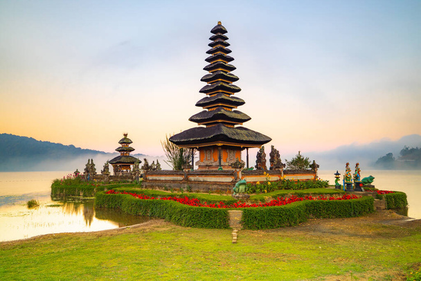 Pura Ulun Danu Bratan Tempel auf der Insel Bali. Schöner balinesischer Tempel. Balinesisches Wahrzeichen. Bewölkter Himmel. Wasserspiegelung. Vorne grünes Gras. Bratan-See, Bedugul, Bali, Indonesien - Foto, Bild