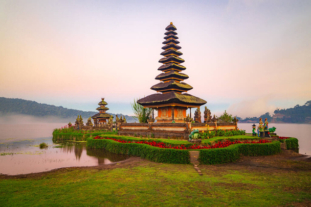 Pura Ulun Danu Bratan Tempel auf der Insel Bali. Schöner balinesischer Tempel. Balinesisches Wahrzeichen. Bewölkter Himmel. Wasserspiegelung. Vorne grünes Gras. Bratan-See, Bedugul, Bali, Indonesien - Foto, Bild