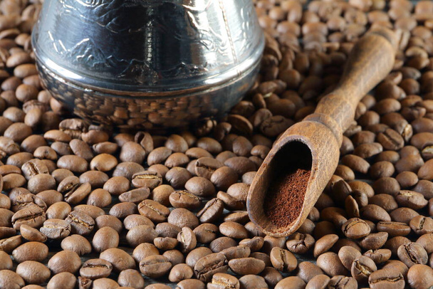Дерев'яна ложка з меленою кавою біля мідної кави серед розсіювання кавових зерен на столі
. - Фото, зображення