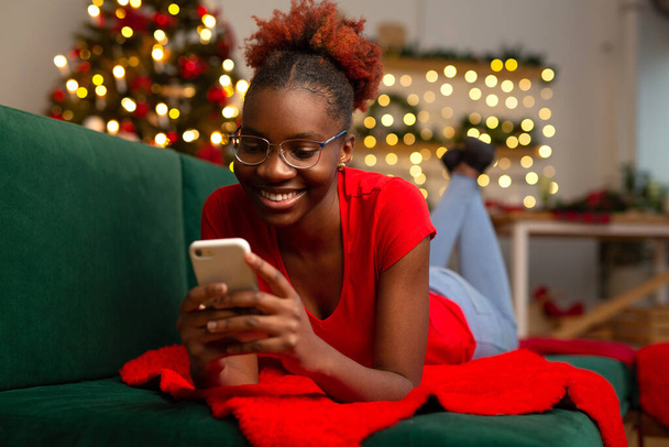 美しい若いアフリカの女性はソファに携帯電話を持っています - 写真・画像