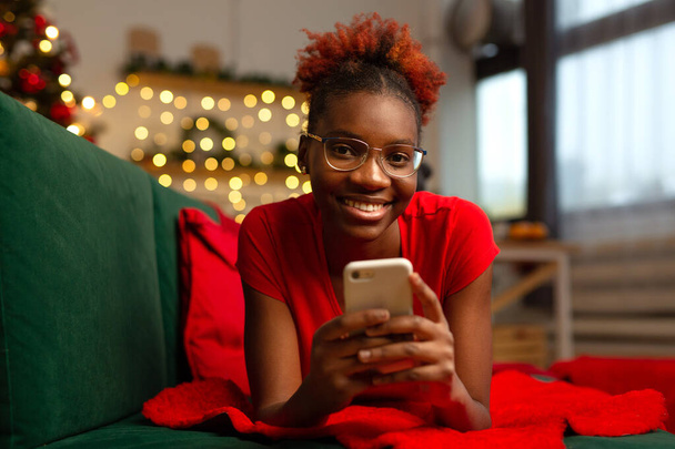 beautiful young african female lies with a mobile phone on the couch - 写真・画像
