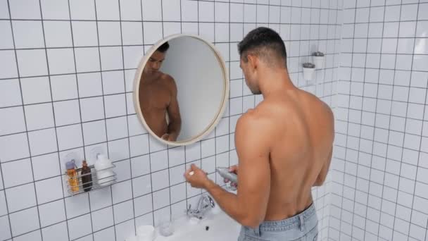 shirtless man spraying deodorant while holding bottle in bathroom - Filmmaterial, Video