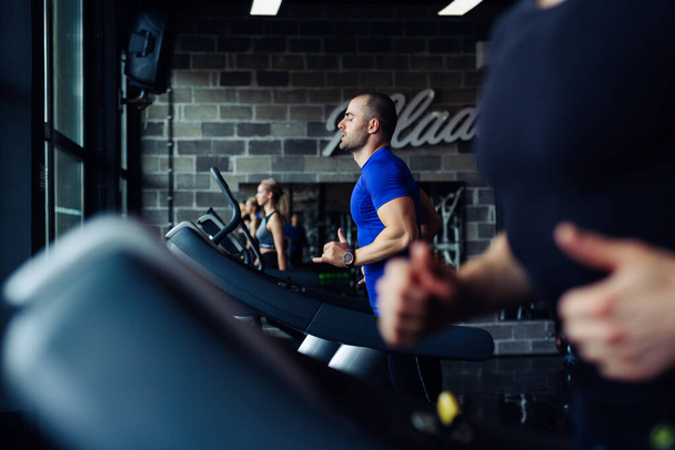 Young man in sportswear running on treadmill at gym. - Valokuva, kuva