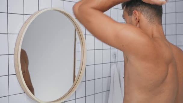 hombre sin camisa rociando desodorante y mirando el espejo en el baño - Imágenes, Vídeo