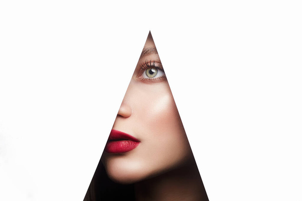 young beautiful woman with a bright makeup. make-up artist concept. A girl with beautiful green eyes, looks into the hole of white paper - Photo, Image
