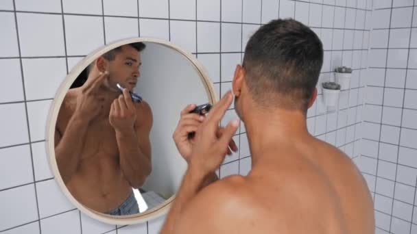 félmeztelen férfi használ trimmer borotválkozás közben a fürdőszobában - Felvétel, videó