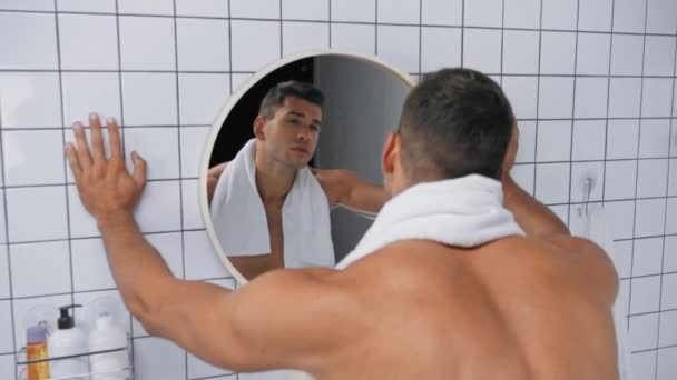 hombre con toalla en el cuerpo sin camisa mirando el espejo en el baño - Imágenes, Vídeo