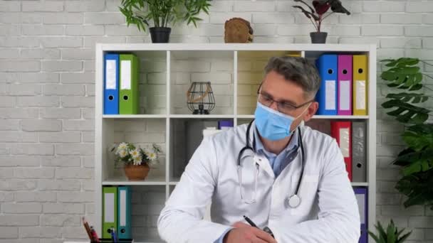 El médico habla escucha al paciente en la oficina del hospital, escribe síntomas en el cuaderno - Imágenes, Vídeo