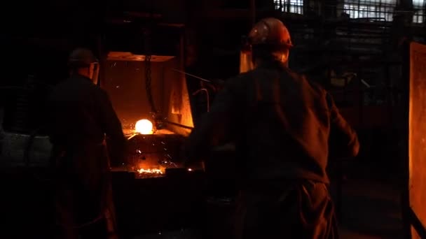 Blacksmiths in a helmet put a piece of hot metal under a mechanical hammer on an anvil. - Footage, Video