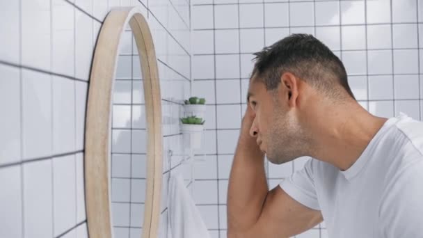 πλαϊνή όψη του άνδρα στερέωση των μαλλιών και ρύθμιση λευκό t-shirt στο μπάνιο - Πλάνα, βίντεο