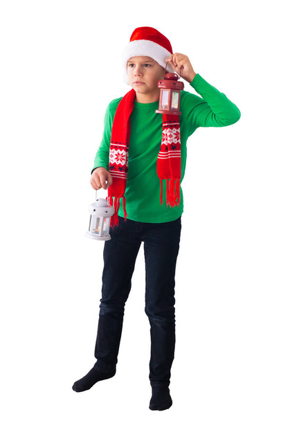 Noel Baba şapkası ve kış eşarbı takan bir çocuğun portresi. Elinde beyaz ve kırmızı fenerler olan korkmuş bir çocuk. Noel zamanı. - Fotoğraf, Görsel