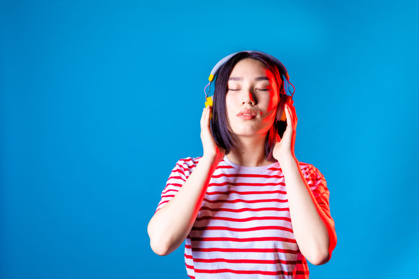 serene asiatic woman isolated on blue  background listening music with bluetooth headphones and eyes closed relaxing  - Foto, immagini