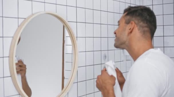 foco de rack de hombre limpiando la cara con toalla cerca del espejo en el baño  - Metraje, vídeo