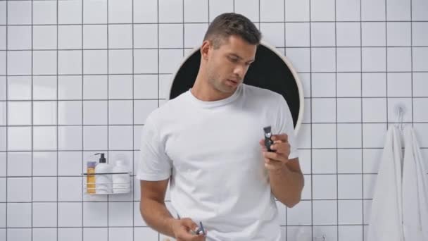 confused man choosing between safety and electric razors in bathroom - Filmmaterial, Video