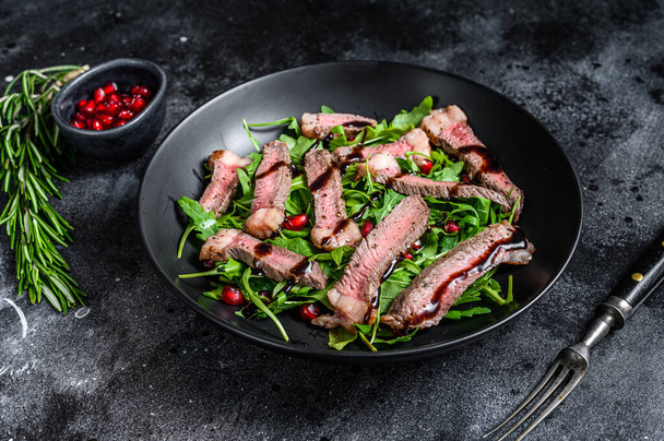 Grillezett marhahús steak saláta arugulával, gránátalmával és zöldséggel. Fekete háttér. Felülnézet. - Fotó, kép