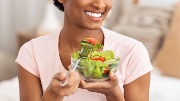 Ausgeschnittene Ansicht einer jungen schwarzen Dame, die drinnen frischen Gemüsesalat isst, Panorama - Foto, Bild