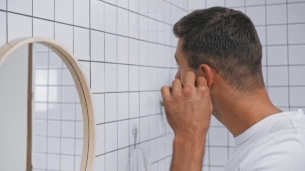 мужчина чистит уши ватным тампоном в ванной комнате  - Кадры, видео