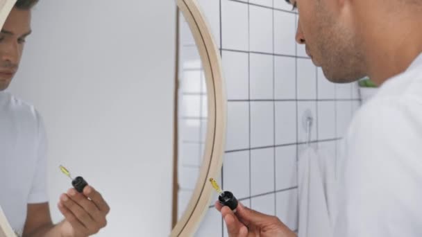 rack focus człowieka stosującego serum na twarz patrząc w lustro  - Materiał filmowy, wideo