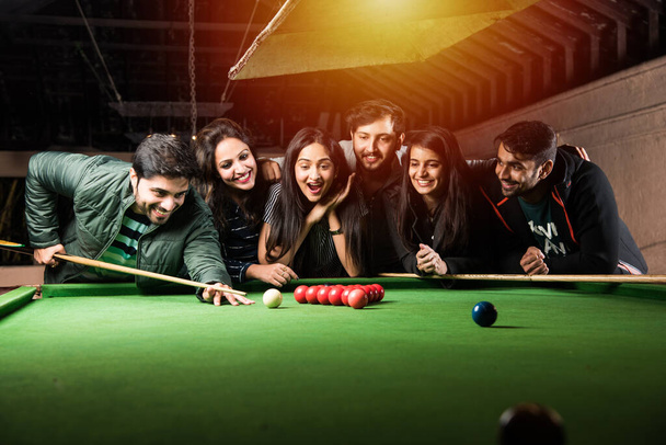 A group of young Indian asian young people or friends playing fun billiards, snooker or pool - Foto, imagen