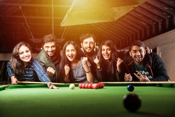A group of young Indian asian young people or friends playing fun billiards, snooker or pool - Photo, Image