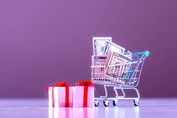 Christmas expense planning concept , gift boxes and shopping cart full of money, image in purple tone - Foto, Bild